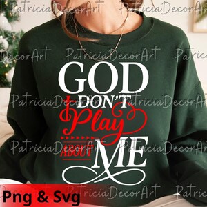 K&ouml;nnte beinhalten: Dunkelgr&uuml;nes Sweatshirt mit dem Text "GOD DON'T PLAY ABOUT ME" in Wei&szlig; und Rot. Das Sweatshirt hat einen Rundhalsausschnitt und lange &Auml;rmel. Der Text ist in einer fetten, stilisierten Schriftart.