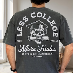 Può includere: T-shirt grigio scuro con grafica sul retro. La grafica presenta un teschio con cappello di laurea e pergamena, circondato dalle parole "LESS COLLEGE" e "MORE TRADES". È presente anche il testo "BLUE COLLAR" e "DIRTY HANDS, CLEAN MONEY".