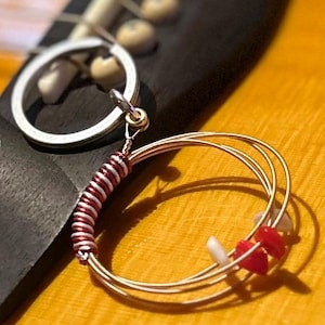 May include: A guitar string keychain with a red and white striped wire wrap and three guitar strings wrapped around a silver key ring.