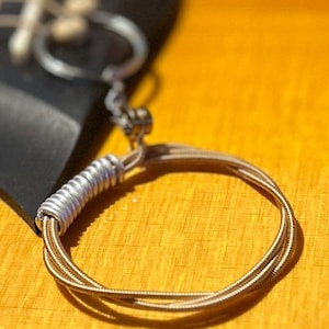 May include: Close-up of a guitar string wound around a metal ring, creating a circular shape. The string is a light brown colour and the ring is silver.