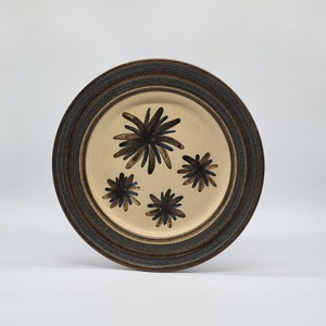May include: A brown and cream ceramic dinner plate with a brown and blue stylised flower design.