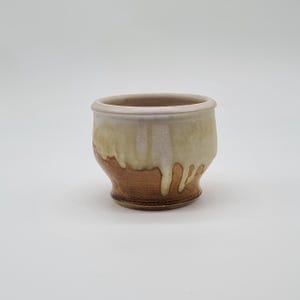 Könnte beinhalten: Eine kleine, weiße Keramikschale mit brauner Glasur auf dem Boden. Die Schale hat eine abgerundete Form und einen leicht ausgestellten Rand.
