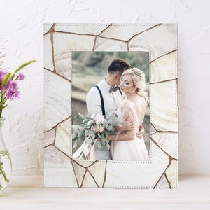 May include: A white picture frame with a stone-like texture and a photo of a couple in a wedding setting. The frame has a white background and a white border.