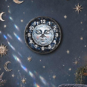 May include: A celestial-themed room with a navy blue wall adorned with gold stars, moons, and a planet. A clock with a moon face hangs above a blue velvet chair with decorative pillows. A stained glass moon hangs in the window.