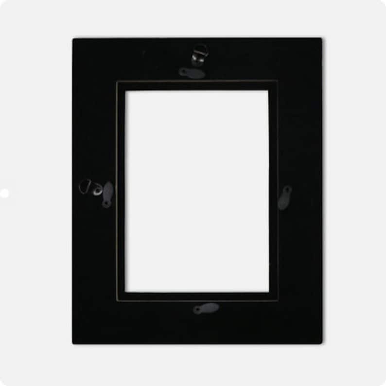 May include: A rectangular black picture frame with a white interior. The frame has a simple, classic design with a flat surface. Metal hardware is visible on the back for hanging. This frame is suitable for displaying photographs or artwork.
