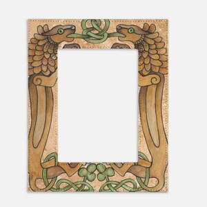 May include: A rectangular picture frame with an intricate Celtic design. Two stylized dragon-like creatures face each other, their tongues intertwined with green knotwork. The frame has a tan background with brown and green accents.
