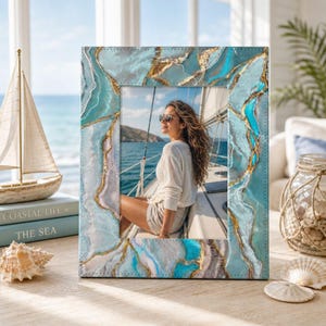 May include: A rectangular picture frame featuring a marbled pattern in shades of turquoise, teal, and white with gold-colored veining. The frame displays a photograph of a person wearing a white long-sleeved shirt and sunglasses on a boat.
