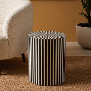 May include: A cylindrical side table featuring a striking black and white striped pattern that runs vertically along the sides and radiates from the center of the top surface in a sunburst design, creating a bold geometric visual effect.