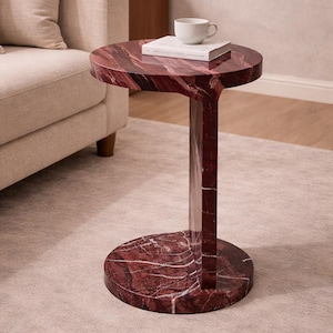 Może przedstawiać: Czerwony marmurowy stolik boczny z okrągłym blatem i podstawą, połączony prostokątną kolumną. Na stole stoi biała filiżanka i książka. Stół stoi obok beżowej sofy.