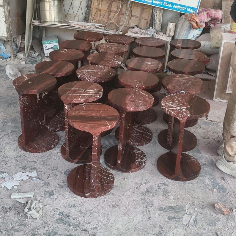 May include: A collection of multiple round side tables crafted from deep red marble with prominent white veining. Each table features a circular top supported by a vertical central pillar and a matching circular base, creating a uniform design.