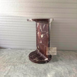 May include: A dark reddish-brown marble side table with white veining, featuring a circular base, a vertical rectangular support column, and a flat circular top. A small square logo with the text CRAFTIFY DECOR is visible on the side.