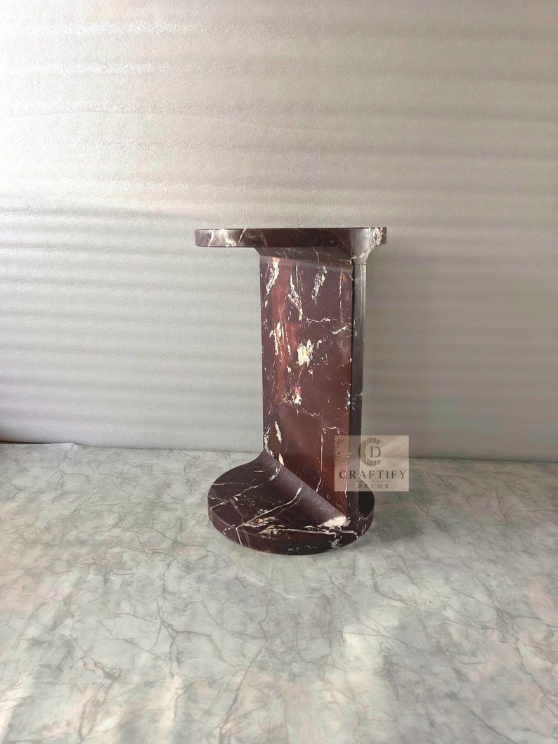 May include: A dark reddish-brown marble side table with white veining, featuring a circular base, a vertical rectangular support column, and a flat circular top. A small square logo with the text CRAFTIFY DECOR is visible on the side.