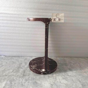 May include: A dark maroon marble side table with white veining, featuring a circular base, a vertical support column, and a round top. A small rectangular tag attached to the top edge displays the text CRAFTIFY DECOR with a circular logo.