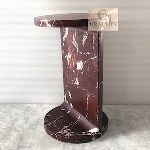 May include: A dark red marble side table with white veining, featuring a circular top and base connected by a vertical rectangular panel. The table has a polished finish and includes a small rectangular logo tag reading CRAFTIFY DECOR.