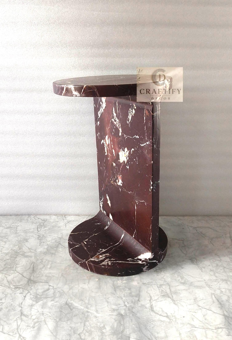 May include: A dark red marble side table with white veining, featuring a circular top and base connected by a vertical rectangular panel. The table has a polished finish and includes a small rectangular logo tag reading CRAFTIFY DECOR.