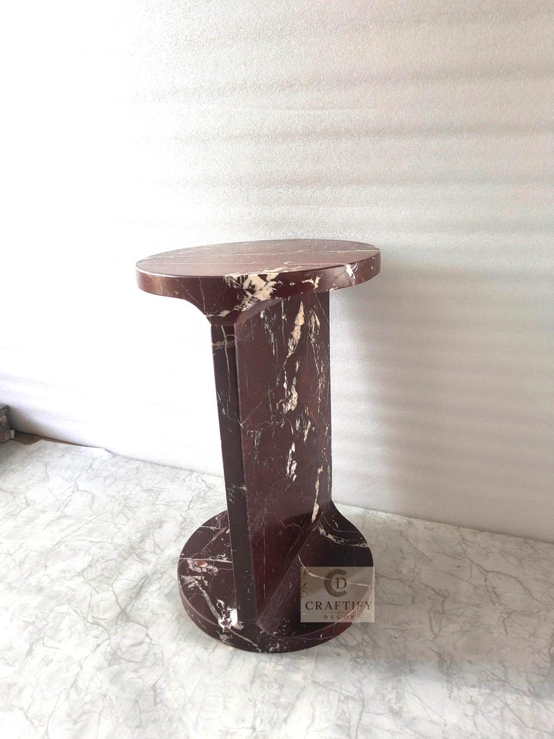 May include: A cylindrical side table crafted from deep red marble with prominent white veining. The piece features a circular top and a matching circular base connected by a vertical central support panel. A small logo reads CRAFTIFY DECOR.