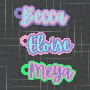 Puede incluir: Tres etiquetas con nombres en capas con una fuente de escritura. La etiqueta superior dice "Becca" en azul, rosa y morado. La etiqueta del medio dice "Eloise" en azul y rosa. La etiqueta inferior dice "Meya" en morado y verde.