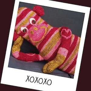May include: A pink and gold striped knitted monkey toy with a big smile and googly eyes. The monkey is holding its arm up in a hug.