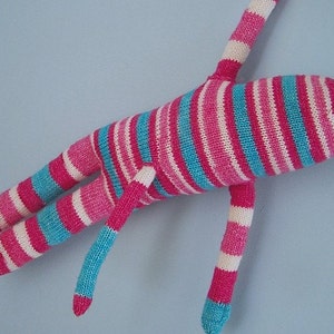 May include: A striped knitted toy with pink, white and blue stripes. The toy has long arms and legs and is lying on a blue surface.