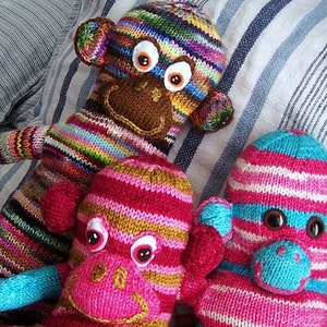 May include: Three knitted toy monkeys with colourful striped patterns and large googly eyes. The monkeys are pink, blue and brown with white stripes.