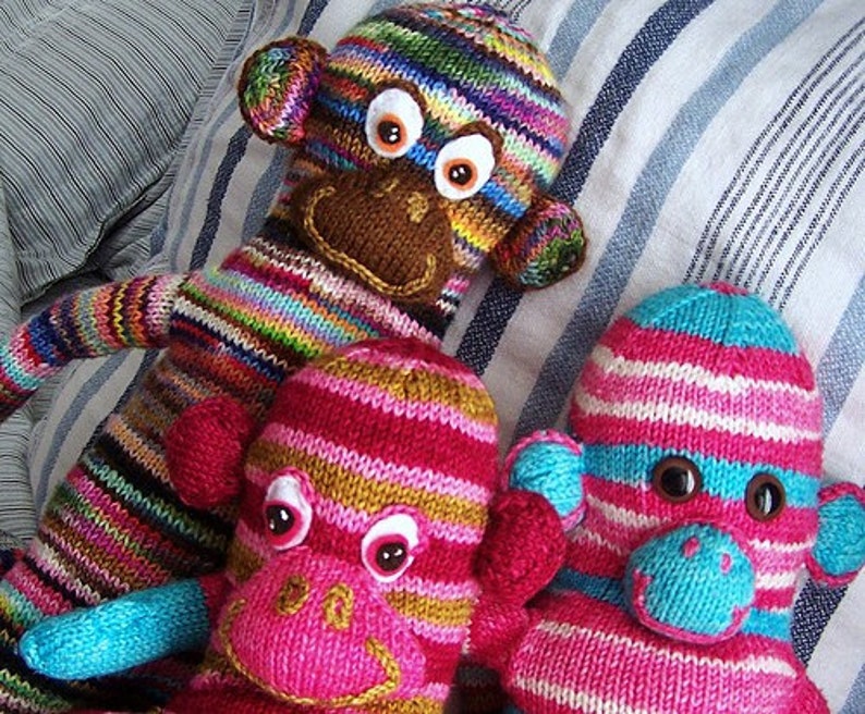 May include: Three knitted toy monkeys with colourful striped patterns and large googly eyes. The monkeys are pink, blue and brown with white stripes.