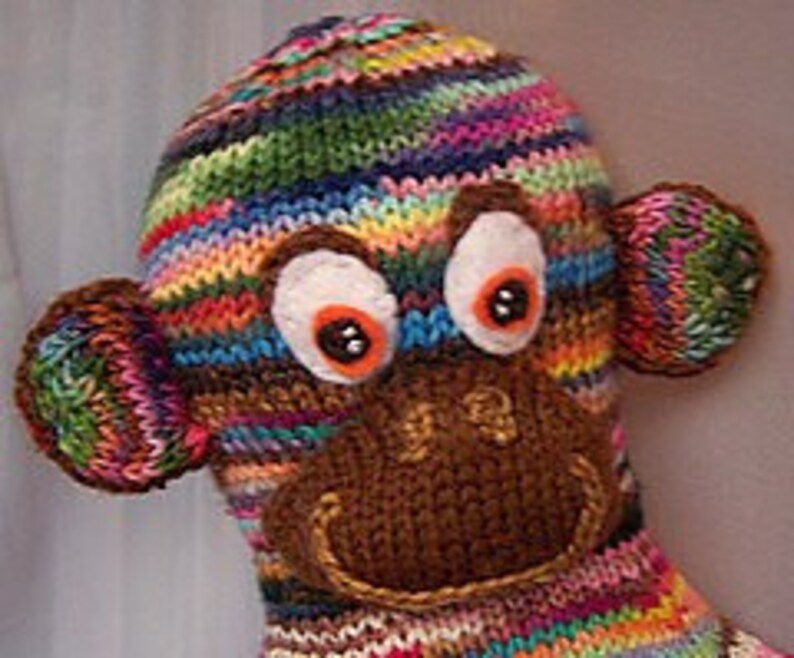 May include: A colourful knitted monkey toy with brown felt ears, a brown felt nose, and large white eyes with black pupils.