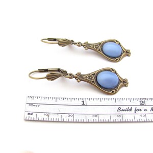 May include: Two antique-style earrings featuring light blue oval stones set in ornate, bronze-coloured metal frames. Each earring is about 3.8 cm long, with lever-back closures. The design incorporates floral details.