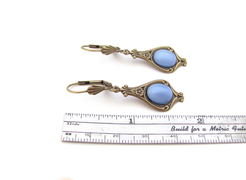 May include: Two antique-style earrings featuring light blue oval stones set in ornate, bronze-coloured metal frames. Each earring is about 3.8 cm long, with lever-back closures. The design incorporates floral details.