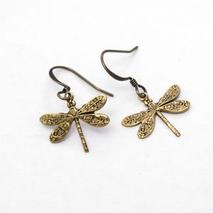 May include: A pair of antique brass-colored dragonfly earrings. Each earring features a detailed dragonfly pendant with etched wings and a long, slender body. The earrings have a simple hook closure.