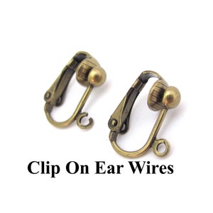 May include: Two antique brass-coloured clip-on earring findings. Each clip has a rounded ball and a hinged clip mechanism. The text "Clip On Ear Wires" is printed in black below the earrings.