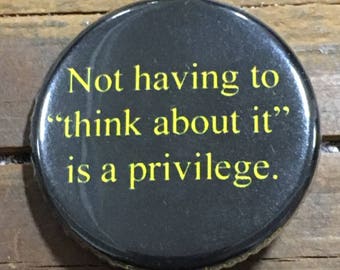 Puede incluir: Botón negro con texto amarillo que dice "No tener que "pensar en ello" es un privilegio."