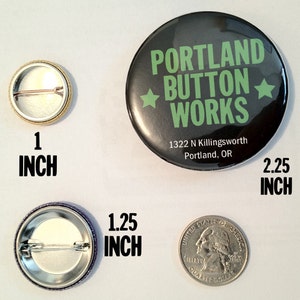 May include: Three different sized button pins. The largest pin is black with white text that reads "PORTLAND BUTTON WORKS" and "1322 N Killingsworth Portland, OR". The pin is 2.25 inches in diameter. The middle pin is 1.25 inches in diameter. The smallest pin is 1 inch in diameter.