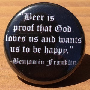 May include: A black button with white text that reads "Beer is proof that God loves us and wants us to be happy."  The text is in a gothic font.  The bottom of the button reads "Benjamin Franklin".