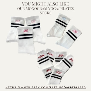 K&ouml;nnte beinhalten: Wei&szlig;e Socken mit zwei schwarzen horizontalen Streifen am B&uuml;ndchen und verschiedenen gestickten Monogrammen oder Namen in rosa, rotem und hellblauem Garn. Der Text lautet: YOU MIGHT ALSO LIKE OUR MONOGRAM YOGA/PILATES SOCKS und eine URL.