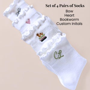 May include: Four pairs of white socks with frilled edges. Each pair has embroidered designs: a bow, heart, bookworm, and custom initials. The image text reads "Set of 4 Pairs of Socks Bow Heart Bookworm Custom Initals."