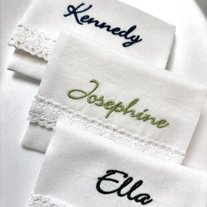 K&ouml;nnte beinhalten: Drei wei&szlig;e Taschent&uuml;cher mit gestickten Namen: "Kennedy" in Marineblau, "Josephine" in Gr&uuml;n und "Ella" in Schwarz. Jedes Taschentuch hat eine zarte Spitzenborte an einer Kante, die einen Hauch von Eleganz verleiht.