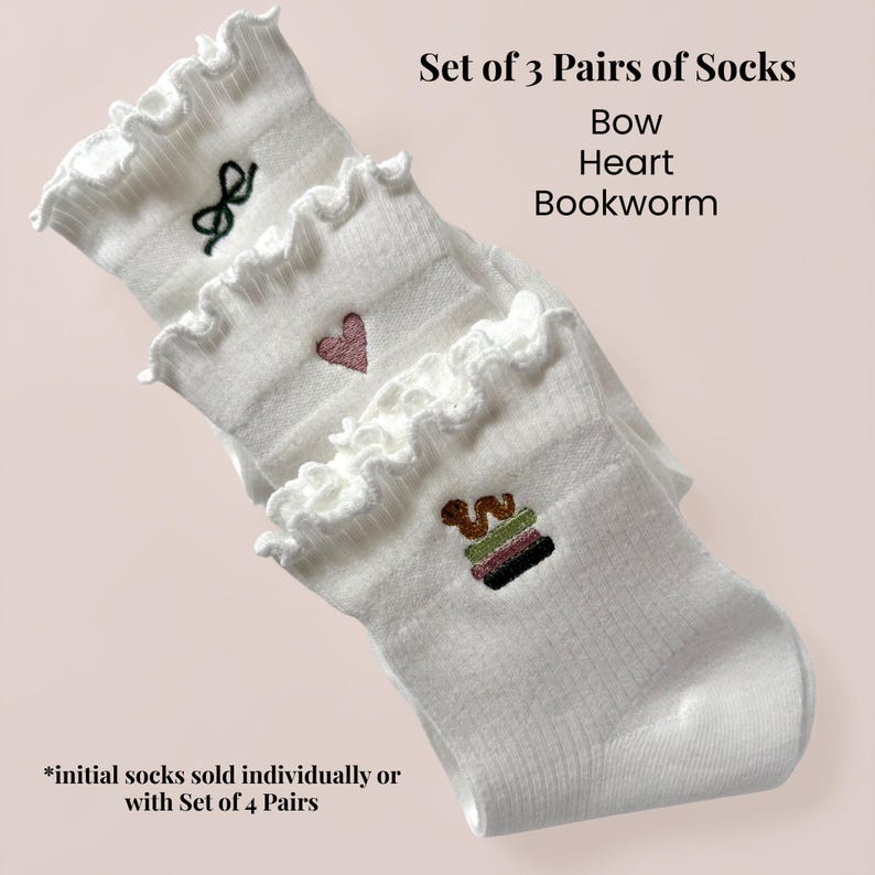 May include: A set of three pairs of white socks with frilled edges. Each pair has embroidered designs: a bow, a heart, and a stack of books. The image text reads "Set of 3 Pairs of Socks Bow Heart Bookworm."