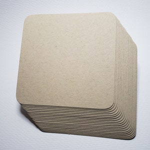 May include: A stack of square, beige cardboard coasters. The coasters are slightly rounded on the edges and have a rough, textured surface.