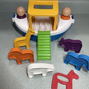 May include: A colorful toy Noah's Ark set with a yellow boat, green ramp, and various animal figures. The set includes a giraffe, hippo, elephant, horse, and two human figures. The boat has a white hull with blue trim.