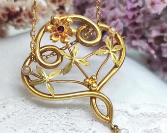 Peut inclure: Un collier pendentif doré avec un motif floral orné. Le pendentif présente une fleur avec un centre rouge, des accents de feuilles et une perle pendante. La chaîne est délicate et le style est vintage.