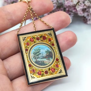 May include: A rectangular pendant with a gold chain. The pendant features a miniature painting of a landscape scene within a black and gold frame, adorned with red rose accents. The chain is also gold.