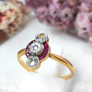 Peut inclure: Bague en or avec un motif central floral serti de petites pierres rouges. La bague comporte deux éléments décoratifs argentés de chaque côté du motif central, chacun orné de petites pierres claires.