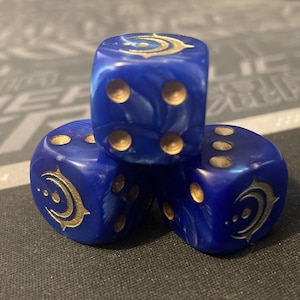 May include: Three blue dice with gold markings and symbols. The dice are stacked, showing different numbers of dots and a crescent moon design. The dice have a marbled effect and are set against a dark background.