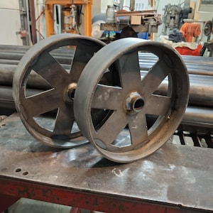 May include: Two large, metal wheels with a starburst design. The wheels are made of a dark metal and have a rough, industrial look.