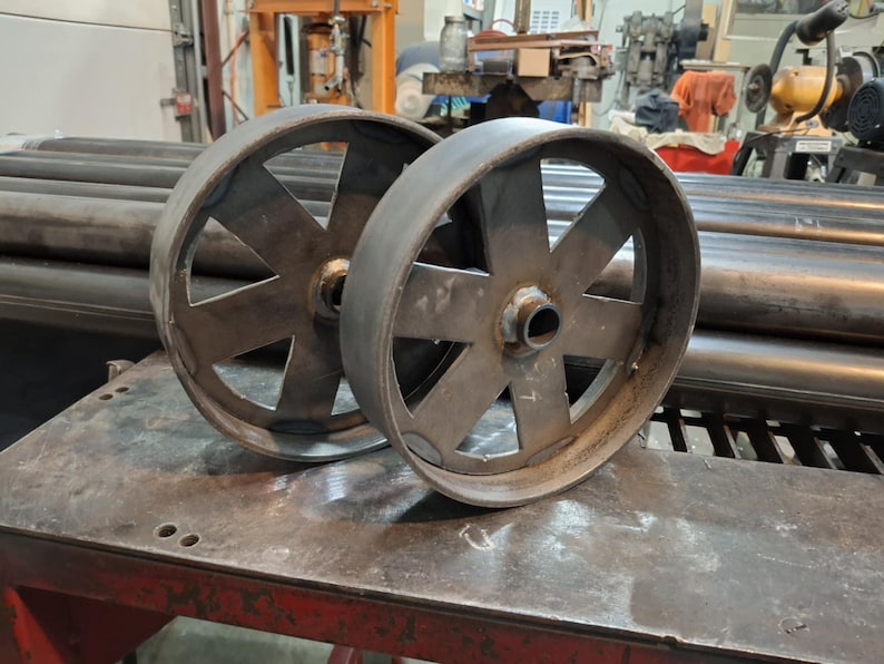 May include: Two large, metal wheels with a starburst design. The wheels are made of a dark metal and have a rough, industrial look.