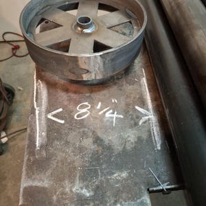 May include: A close-up of a metal wheel with six spokes. The wheel is 8 1/4 inches in diameter and is sitting on a metal surface.