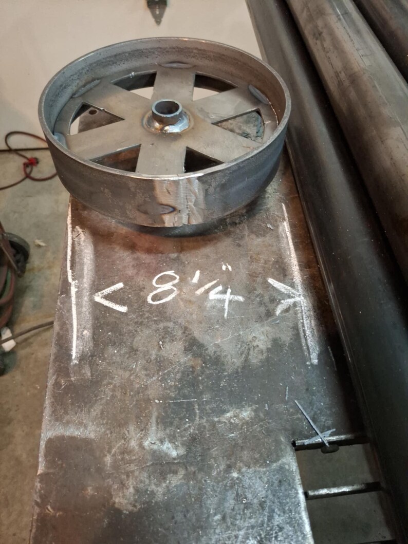 May include: A close-up of a metal wheel with six spokes. The wheel is 8 1/4 inches in diameter and is sitting on a metal surface.
