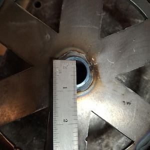 May include: Close-up of a metal disc with six cutouts, a ruler measuring 3 inches, and a circular hole in the center.