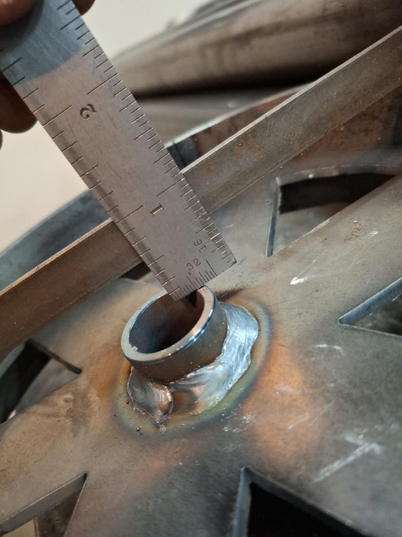May include: Close-up of a metal pipe with a ruler measuring the diameter of the pipe. The pipe is welded to a metal plate with a star-shaped cutout.