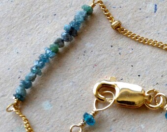 May include: A gold chain necklace with a delicate chain and small beads. The necklace features a long strand of blue and green gemstones.